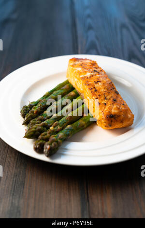 Weiße Platte mit gebratenem Lachsfilet mit gebratenem Spargel auf einem dunklen Hintergrund Stockfoto