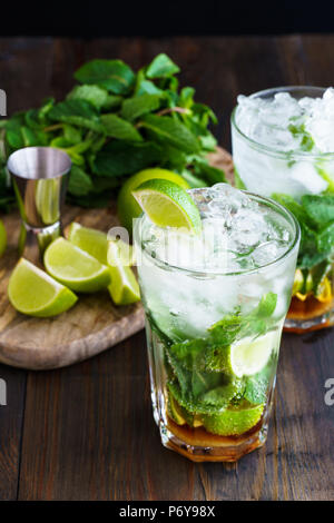 Dirty Mojito und Zutaten (frische Minze, geschnitten Kalk) auf einem dunklen Holzbrett serviert. Hohe Auflösung. Stockfoto