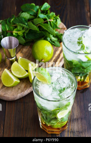 Dirty Mojito und Zutaten (frische Minze, geschnitten Kalk) auf einem dunklen Holzbrett serviert. Hohe Auflösung. Stockfoto