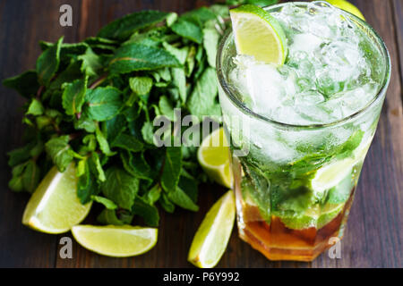 Dirty Mojito und Zutaten (frische Minze, geschnitten Kalk) auf einem dunklen Holzbrett serviert. Hohe Auflösung. Stockfoto