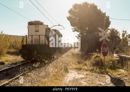 Bahnübergang ohne Barrieren mit einem Stoppschild, während ein Güterzug. Sagunto, Valencia, Spanien