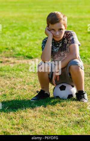 Traurig Suche pre-teen Junge sitzt auf einer Kugel. Verlorene Spiel oder nicht für ein Team Konzept abgeholt Stockfoto