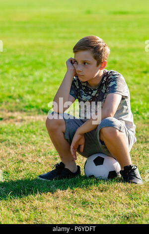 Traurig Suche pre-teen Junge sitzt auf einer Kugel. Verlorene Spiel oder nicht für ein Team Konzept abgeholt Stockfoto