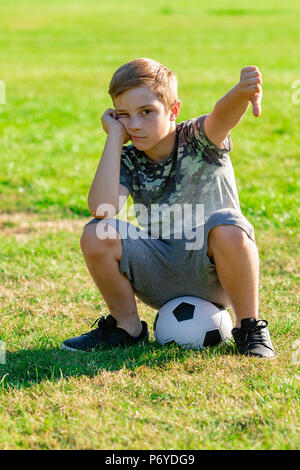 Traurig Suche pre-teen Junge sitzt auf einer Kugel. Verlorene Spiel oder nicht für ein Team Konzept abgeholt Stockfoto