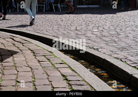 Beine von Menschen zu Fuß neben Bächle, Wasser - Bächlein in der Fußgängerzone in der Altstadt von Freiburg, Deutschland Stockfoto