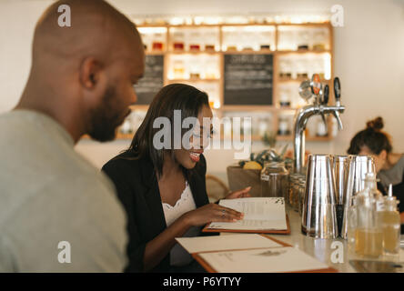 Lächelnden jungen afrikanischen amerikanischen Paar lesen Menüs in einer Bar Stockfoto