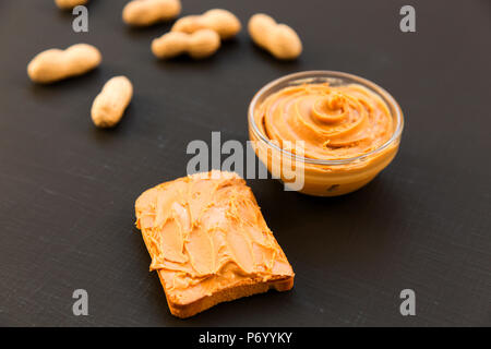 Schüssel mit Erdnussbutter, ohne schale Erdnüsse auf schwarzem Hintergrund, Seitenansicht. Stockfoto