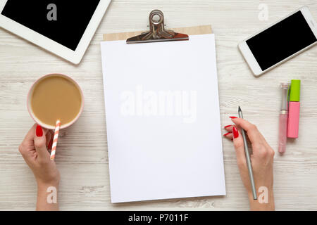 Feminine Arbeitsbereich mit Tablet, noticepad, Blatt, Latte, Smartphone und weibliche Hände über weiß Holz- Hintergrund, Ansicht von oben. Stockfoto