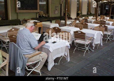 Ein Mann arbeitet allein in ein Restaurant am Fluss auf Cankarjevo Nabrezje in der slowenischen Hauptstadt Ljubljana, am 25. Juni 2018 in Ljubljana, Slowenien. Stockfoto