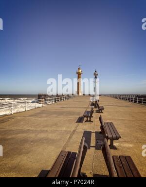 Am Pier in Whitby in den frühen Morgen. Es gibt Sitzplätze sind im Vordergrund und der Leuchtturm in der Ferne. Stockfoto