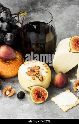 Snacks mit Wein - verschiedene Arten von Käse, Feigen, Nüsse, Honig, Trauben auf grauem Hintergrund Stockfoto