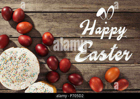 Blick von oben auf die Ostern Kuchen, bemalte Eier und frohe Ostern Inschrift auf Holz- Oberfläche Stockfoto