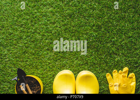 Blick von oben auf die gelbe Gummistiefel, Handschuhe und Blumentopf mit Gartengeräte Stockfoto