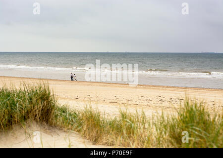 Zwei Menschen zu Fuß entlang der floodline an einem bewölkten Tag an der Westküste der Niederlande. Mit Dünen, Sand, Strand, Meer und Himmel. Stockfoto