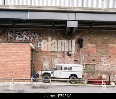 Unterhalb der Straße Überführung, zwei Arbeiter in der ouseburn Bezirk von Newcastle-on-Tyne halten Dinge arbeiten - eine Reparatur ein Land Rover, die anderen repoints ein Stockfoto