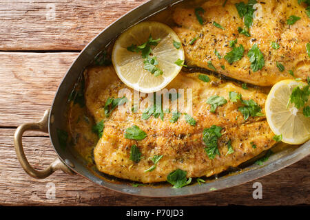 Gebackene Forelle Fisch mit Knoblauch Zitrone Butter, Petersilie closeup in einem Kupfer Pfanne auf dem Tisch. horizontal oben Ansicht von oben Stockfoto