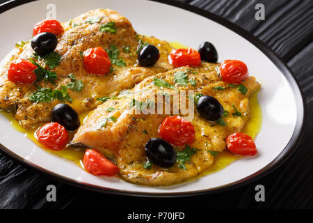 Italienisches Essen: Gebratene Forelle Filets mit Knoblauch Zitrone butter Soße, Tomaten, Petersilie und Oliven close-up auf einem Teller auf dem Tisch. Horizontale Stockfoto