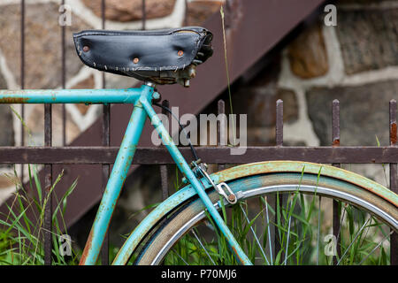 Nahaufnahme eines Fahrrades und Sitz gelehnt auf einem rostigen Zaun. Stockfoto