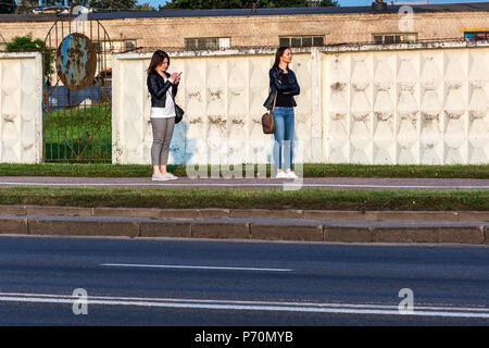 Belarus, Minsk - September 09, 2017: Zwei Mädchen stehen auf dem Bürgersteig in der Nähe des Zauns. Ein Mädchen in die Ferne schaut, das zweite Mädchen sucht in Stockfoto