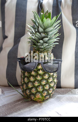 Ananas Obst mit schwarzem Kunststoff Sonnenbrille vor abgestreift Strand Kissen Stockfoto