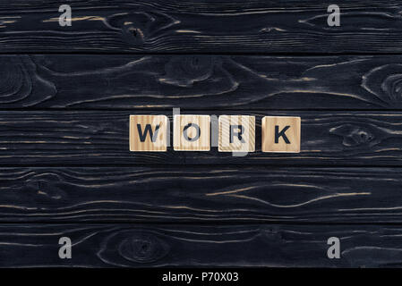 Draufsicht auf das Wort Arbeit aus Holzklötzen auf dunklen, hölzernen Tischplatte Stockfoto