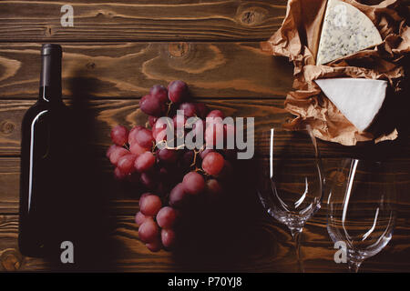 Blick von oben auf die Flasche Rotwein mit Brille und Aperitifs auf hölzernen Tisch Stockfoto