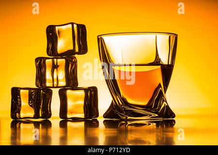 Glas mit Whiskey und Eis in der Nähe von auf orange Hintergrund Stockfoto