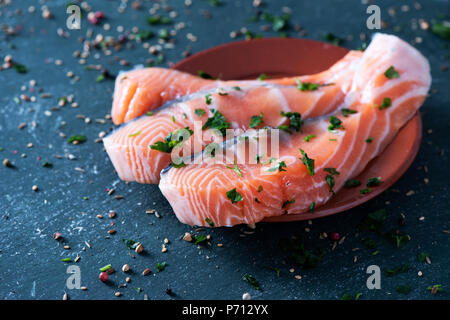 Nahaufnahme von einigen rohen Lachs auf weißem Marmor Fach, auf einem dunklen rustikale Oberfläche bestreut mit Kräutern und Gewürzen Stockfoto