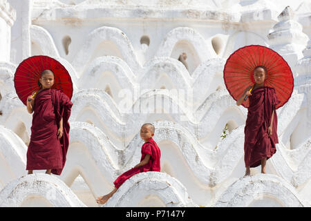 Drei junge Mönche in rot gekleidet, mit roten Sonnenschirme am Myatheindan Pagode (weiße Tempel) in Mingun, Myanmar (Burma), Asien Stockfoto