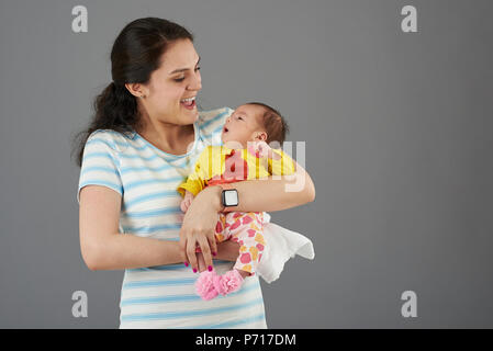 Lachende junge Hispanic Mutter mit Baby girl portrait auf grauem Hintergrund Stockfoto