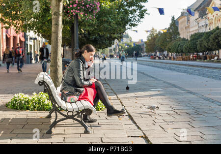 KOSICE, SLOWAKEI - Oktober 02, 2017: Unbekannte schöne junge Frau sitzt mit Smartphone auf der Bank in der Altstadt. Die größte Stadt im östlichen Slo Stockfoto