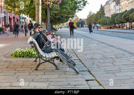 KOSICE, SLOWAKEI - Oktober 02, 2017: Unbekannte schöne junge Frau sitzt mit Smartphone und Fahrrad auf der Bank in der Altstadt. Kosice City war das Stockfoto