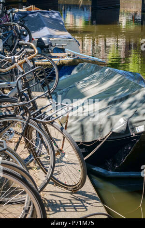 Fahrräder und Boote in hellem Sonnenlicht neben einem Kanal in Amsterdam. Stockfoto