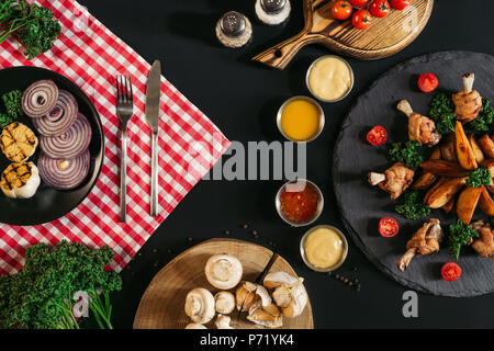 Blick von oben auf die verschiedenen Saucen, Bratkartoffeln mit Hähnchen und Gemüse auf Schwarz Stockfoto