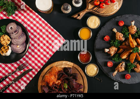 Blick von oben auf die Gourmet verschiedene Fleisch, Gemüse, Saucen und gebackene Kartoffeln mit gerösteten Hähnchen auf Schwarz Stockfoto