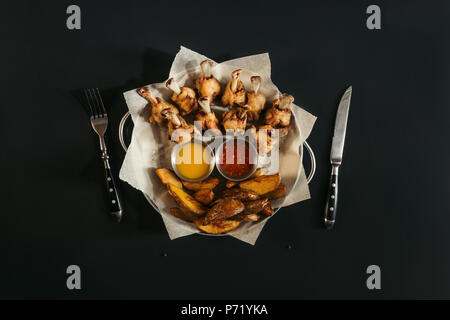 Blick von oben auf die köstliche gebackene Kartoffeln mit Saucen und gerösteten Chicken Wings auf Schwarz Stockfoto