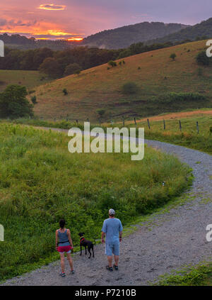 Paar Wandern Blue Ridge Mountain Sunset - Sonnenuntergang auf dem Blue Ridge Parkway. Golden Sky mit Wanderweg, Kühe und Nebel in der Ferne. Stockfoto