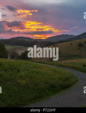 Blue Ridge Mountain Sunset - Sonnenuntergang auf dem Blue Ridge Parkway. Golden Sky mit Wanderweg, Kühe und Nebel in der Ferne. Während der sommersonnenwende. Stockfoto