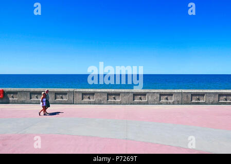 Paar mittleren Alters legere Sommerkleidung zu Fuß entlang der Strandpromenade in Blackpool an einem heißen sonnigen Tag Stockfoto