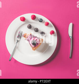 Blick von oben auf die gebissen Stück Kuchen mit Beeren auf Platte auf rosa Oberfläche Stockfoto