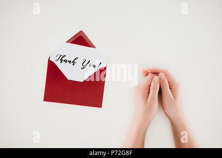 7/8 Schuß von Frau halten sich an den Händen in der Nähe von roten Umschlag mit vielen Dank Schriftzug auf dem Papier isoliert auf weißem geöffnet Stockfoto