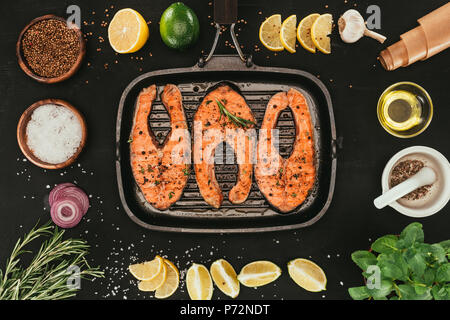 Blick von oben auf die lachssteaks auf Grill und Gewürzen auf Schwarz Stockfoto