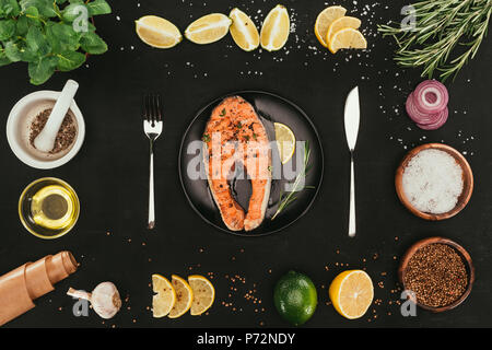 Blick von oben auf die lachssteak mit Besteck und Gewürze auf Schwarz Stockfoto