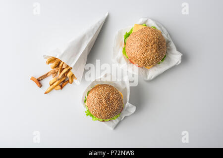 Blick von oben auf die Pommes frites in Papiermembran und zwei Burger, isoliert auf weißem Stockfoto
