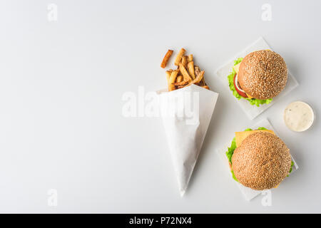 Blick von oben auf die Pommes frites in Papiermembran, zwei Hamburger und Mayonnaise, isoliert auf weißem Stockfoto