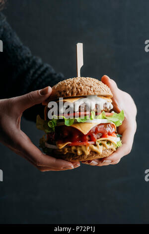 Blick auf weibliche Hände mit großen selbstgemachte Cheeseburger 7/8 Stockfoto