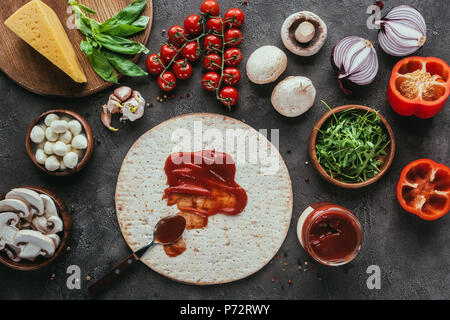 Blick von oben auf die Pizza Teig mit gegossen, Ketchup und verschiedene Gemüse auf konkrete Tabelle Stockfoto