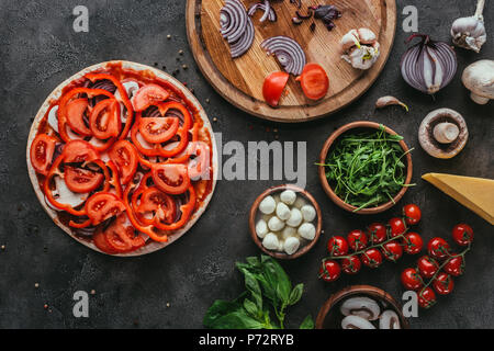 Blick von oben auf die rohe Pizza mit unterschiedlichen Zutaten auf konkrete Tabelle Stockfoto