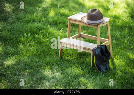 Nahaufnahme der angeordneten schwarzen Leder Schuhe und Strohhut auf hölzernen Treppen auf Grünland Stockfoto