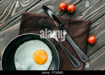 Pfanne mit Ei und Besteck auf Holztisch mit Tomaten Stockfoto